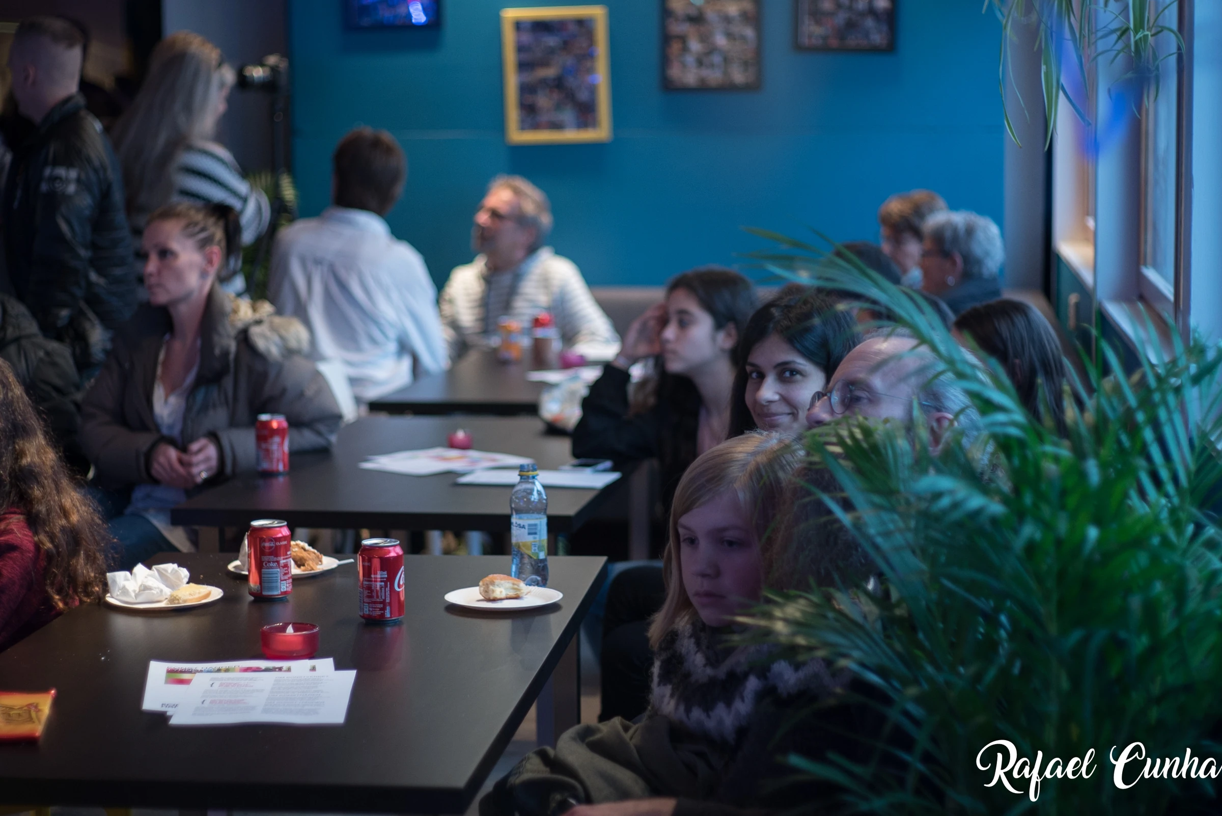 Visitors sit at tables in a café with blue walls, with soft drinks and pastries in front of them.