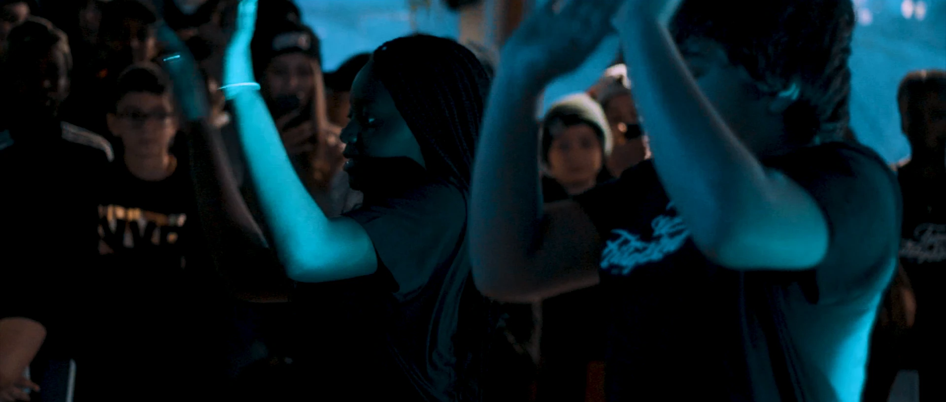 An audience in blue light claps with their hands in the air.
