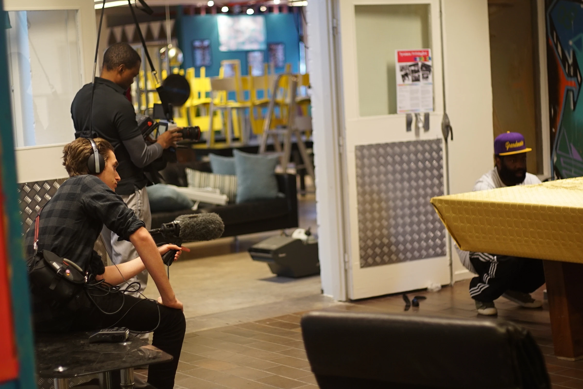 A camera operator and a sound technician with a boom microphone film a scene at a table with a gold-coloured cloth.