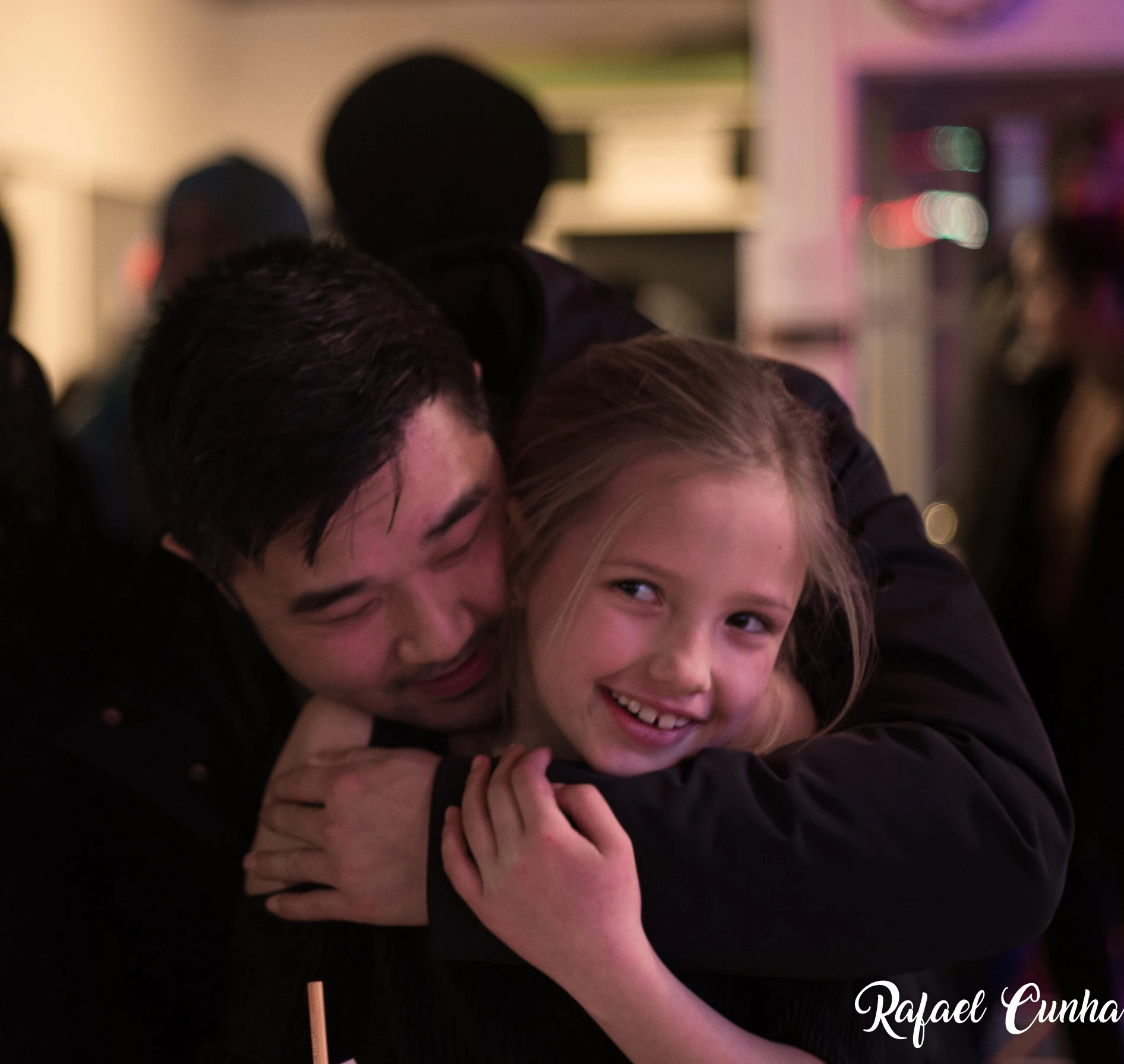 An adult hugs a smiling child from behind.