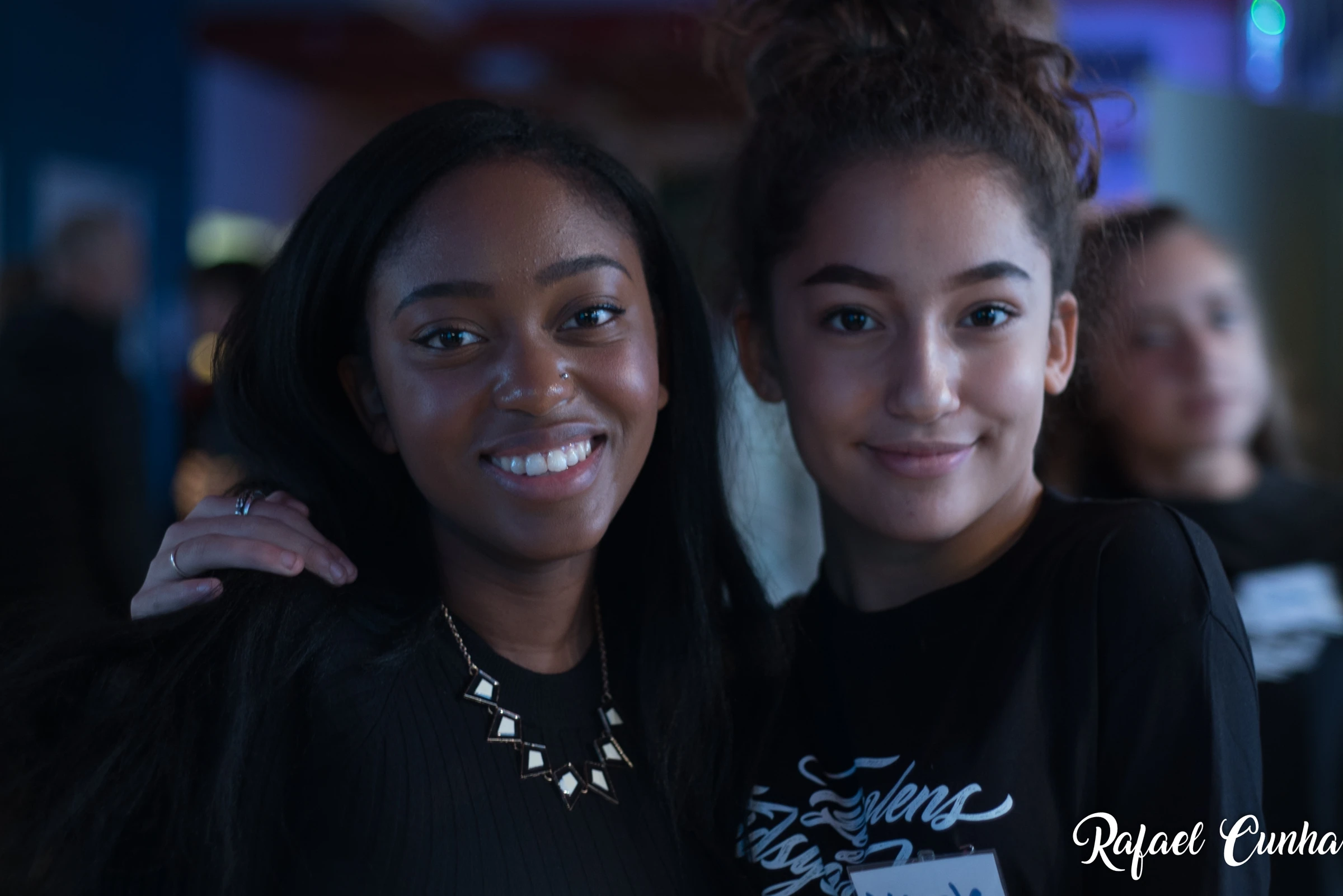 Two young women stand close together and smile at the camera.