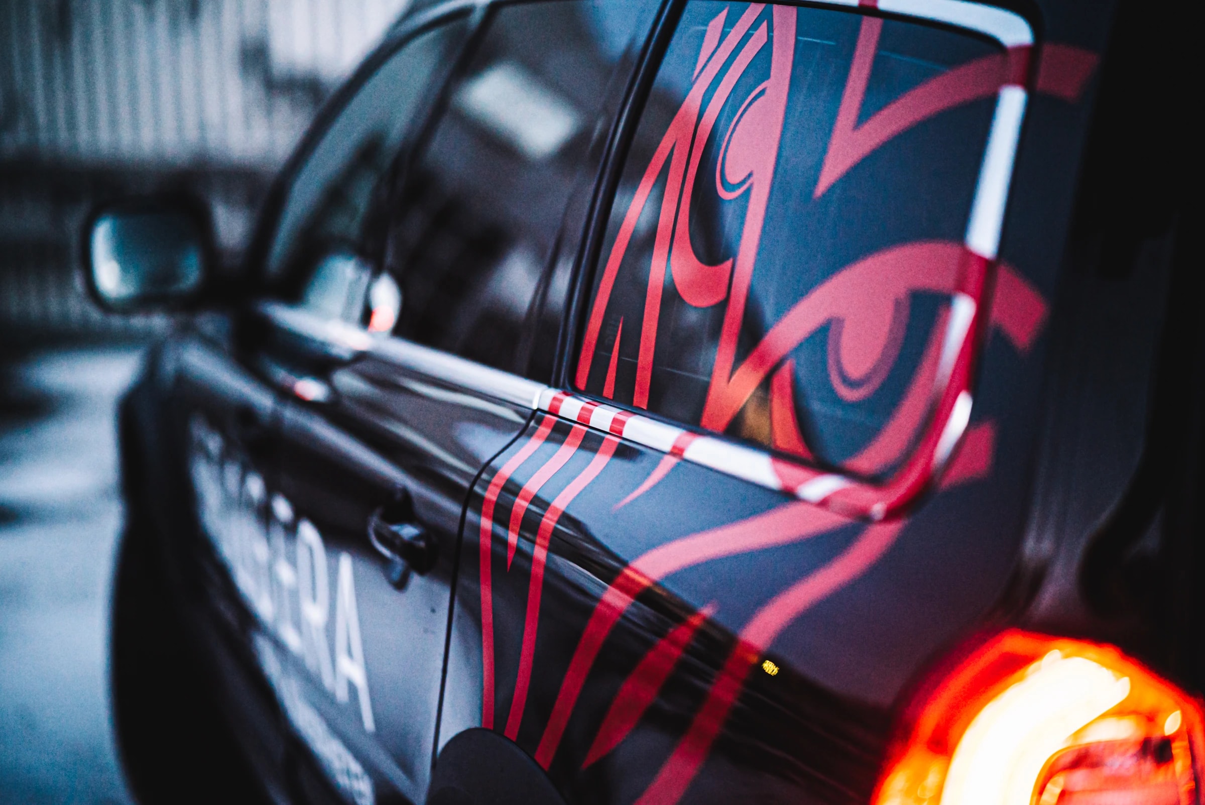 Close-up of the side of a black car, where a large red owl in vinyl stretches across the rear door and window.