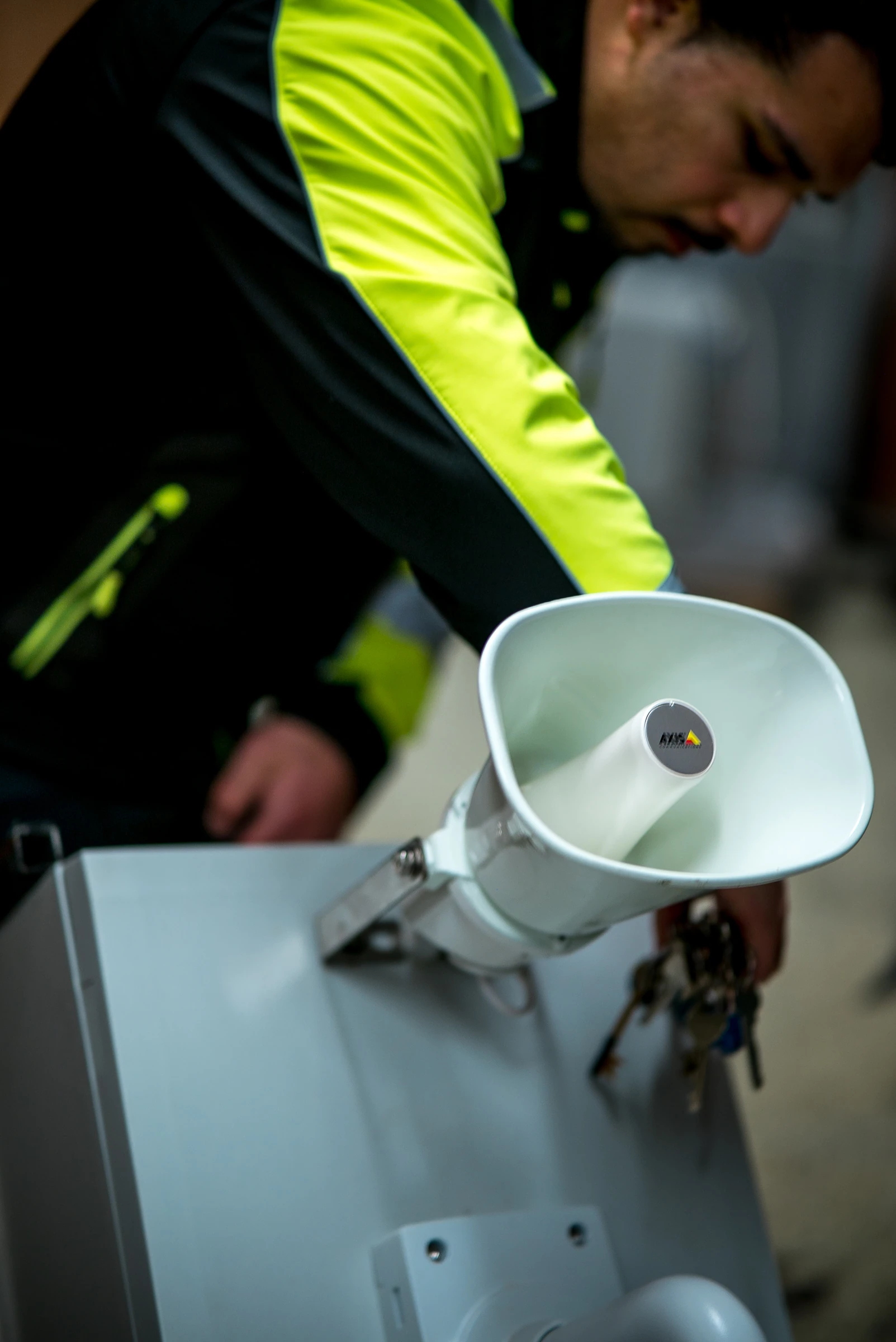 A technician in a Seagera jacket holds a white speaker on a bracket.