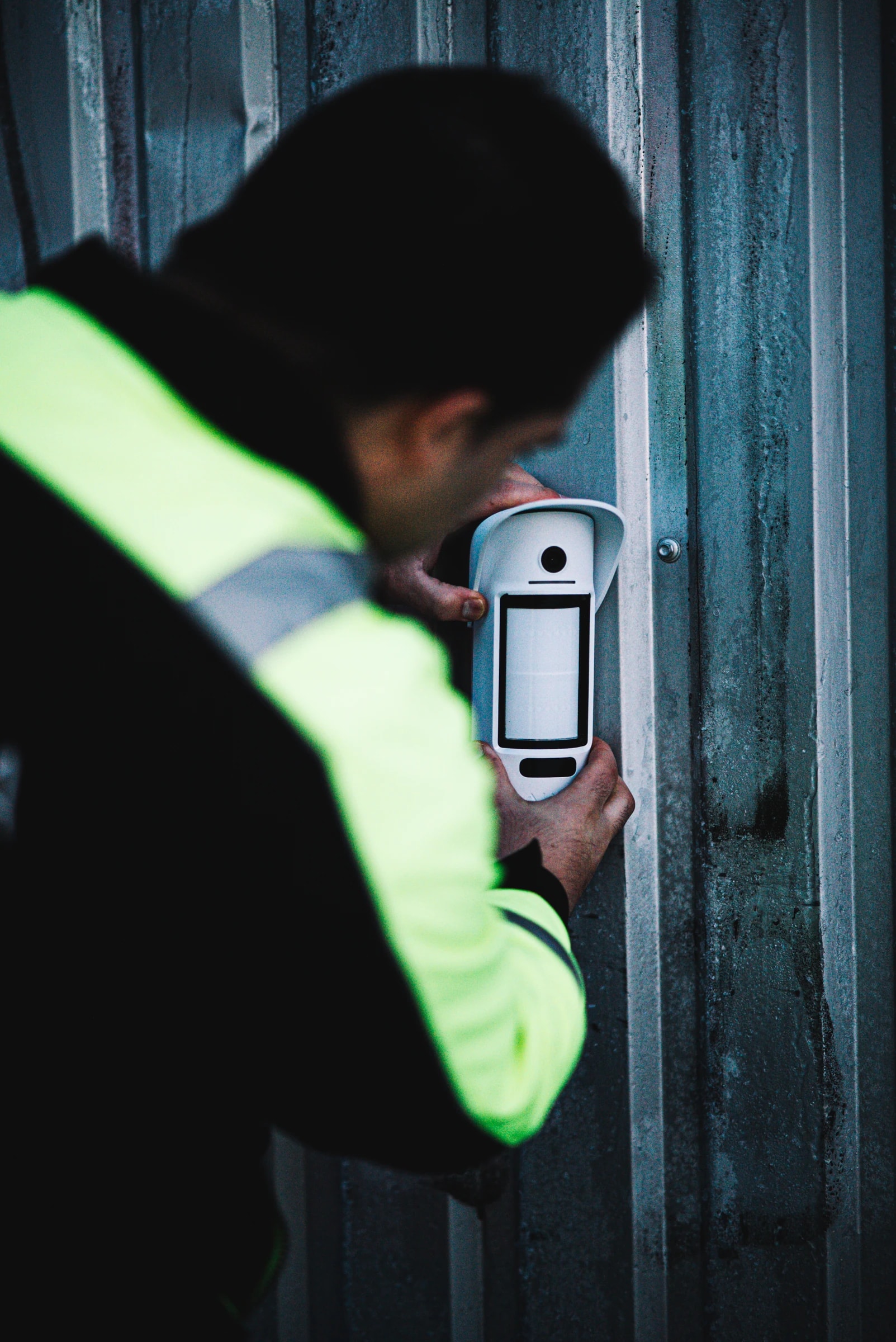 A technician in high-visibility clothing fits a camera detector to a wall.