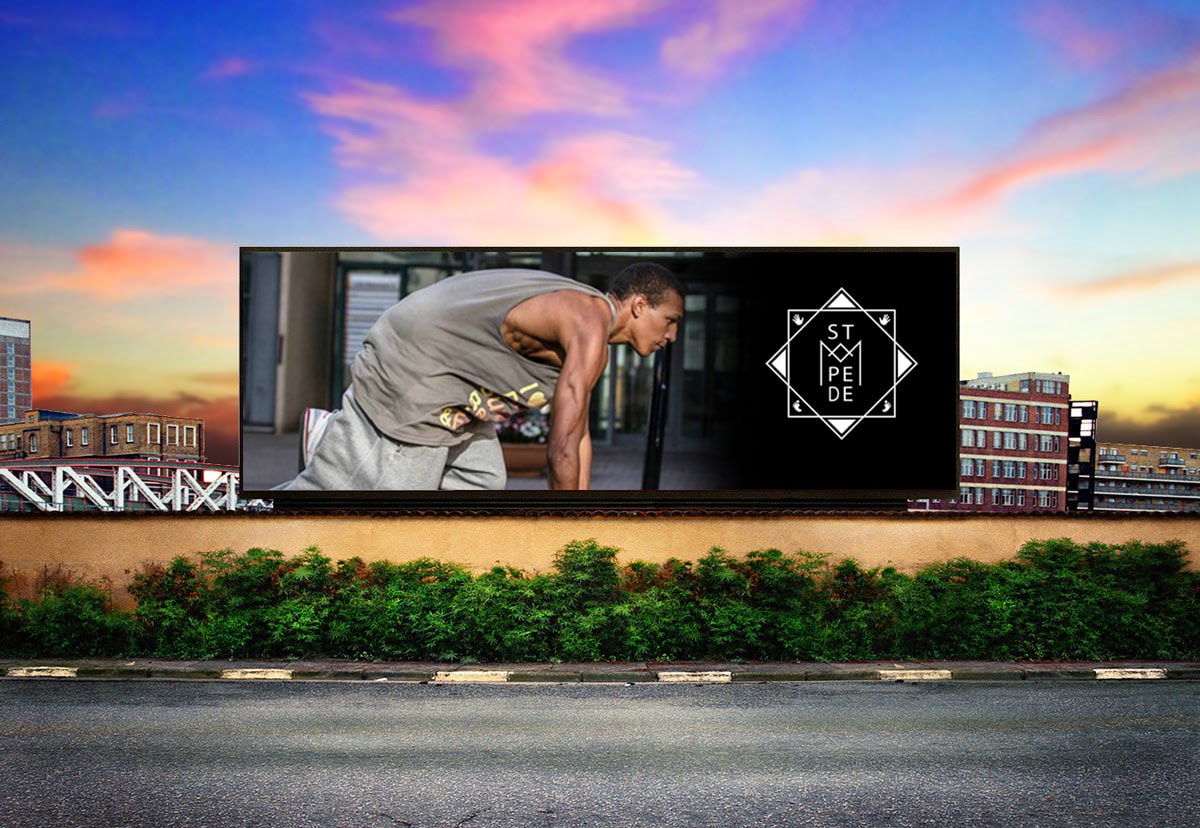 A roadside billboard at sunset. On it, a person in a starting position on the left and the Stampede logo in white on black on the right.